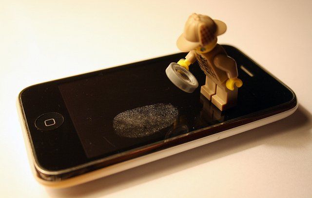 Une empreinte de doigt sur un téléphone portable, scrutée par une figurine tenant une loupe.