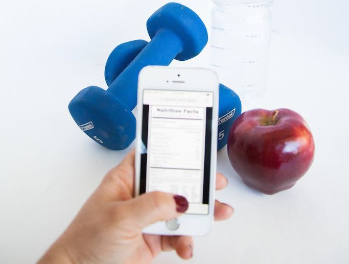 Un smartphone devant des petites haltères et une pomme.